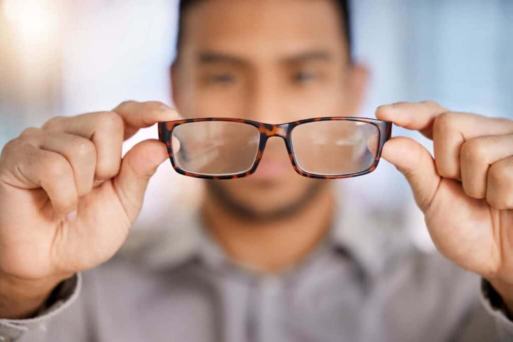 how to keep your eyeglasses clean, man holding glasses